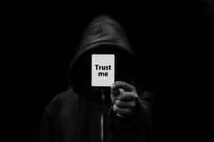 Persoon in een donkere capuchontrui houdt een kaartje met de tekst Trust me omhoog
