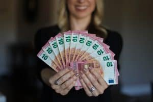 Vrouw houdt lachend een waaier van briefjes van tien euro voor zich
