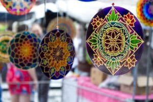 Beschilderde glazen mandala’s in paars, geel en groen hangen te koop aan een marktkraam
