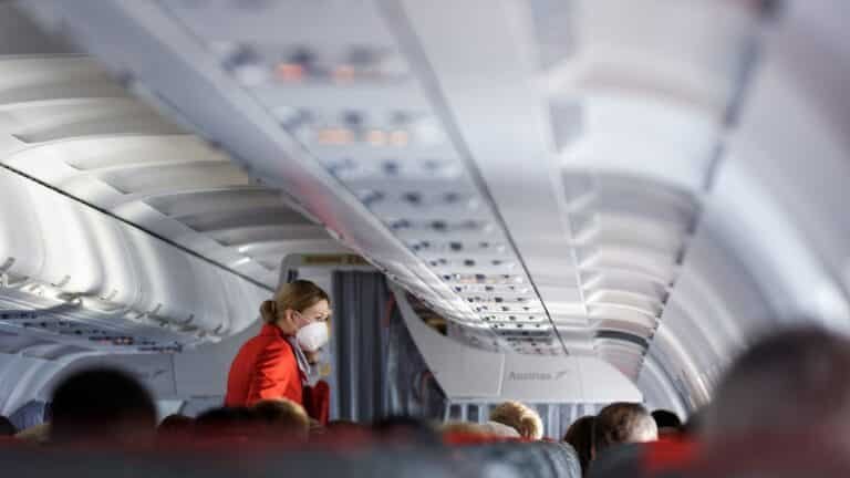 Stewardess met mondkapje loopt door het gangpad van een vliegtuig