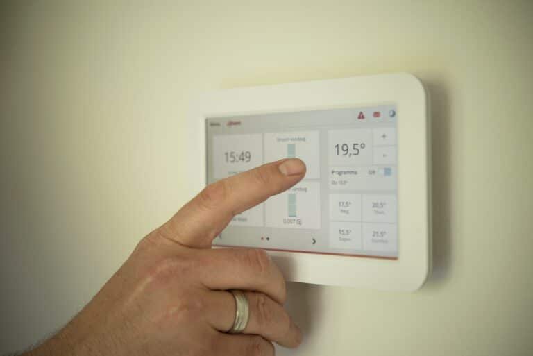 Hand bedient een thermostaat aan de muur die 19,5 graden aangeeft