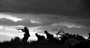 Silhouetten van soldaten met geweren tegen een donkere lucht, in zwart-wit