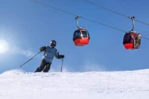 Skiër op een zonnige piste met rode gondels van een kabelbaan erboven