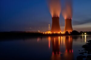 Twee koeltorens van een kerncentrale met stoompluimen, weerspiegeld in het water bij schemering
