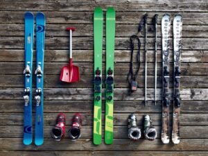 Ski's, skistokken, skischoenen en een lawineschep naast elkaar op een houten vloer