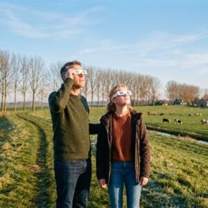 Vader en dochter op een dijk kijken op een heldere herfstochtend met kartonnen eclipsbrillen omhoog naar de zon