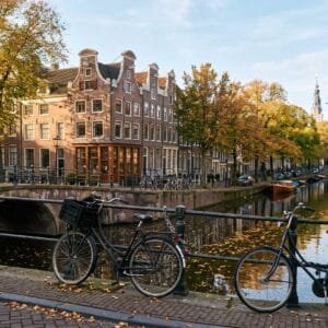Smalle koopmanshuizen met trapgevels en halsgevels langs een Amsterdamse gracht op een zonnige herfstochtend