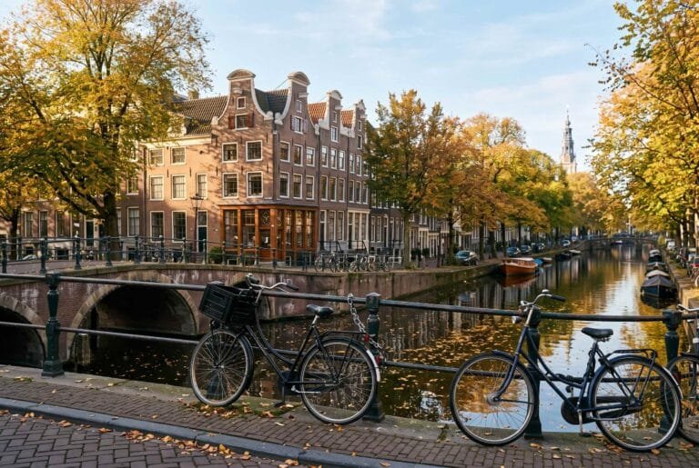 Smalle koopmanshuizen met trapgevels en halsgevels langs een Amsterdamse gracht op een zonnige herfstochtend