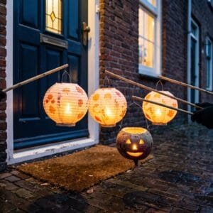 Papieren lampionnen en een uitgeholde biet met een kaars bij de voordeur van een rijtjeshuis op een novemberavond