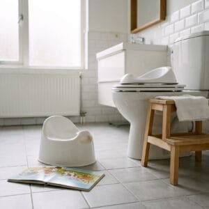 Plastic potje en prentenboek op de badkamervloer naast een wc met verkleiner op de bril en een opstapje