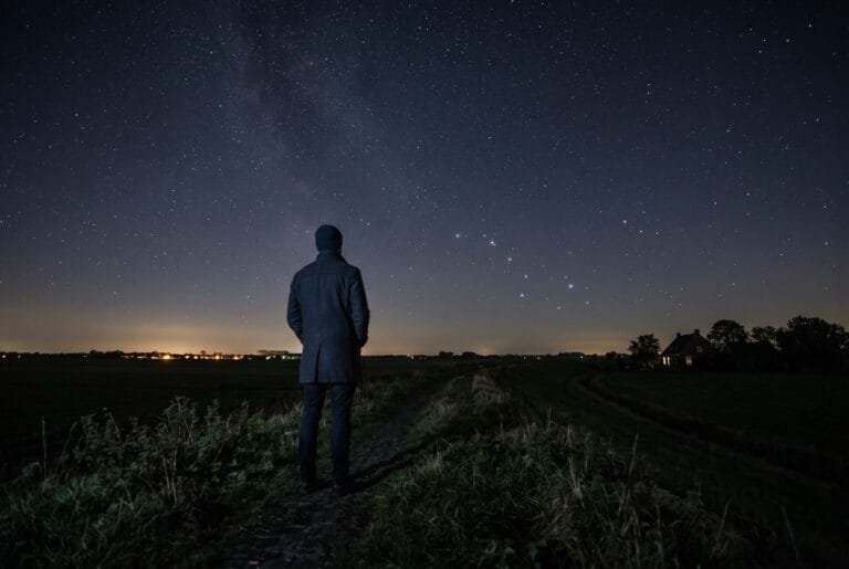 Wandelaar op een dijk kijkt in een heldere nacht naar de sterren boven een vlakke polder