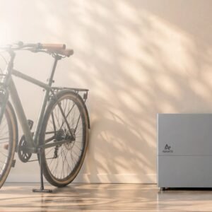 Grijze AlphaESS VitaPower thuisbatterij van 8 kWh op een lichte vloer naast een stadsfiets in de ochtendzon