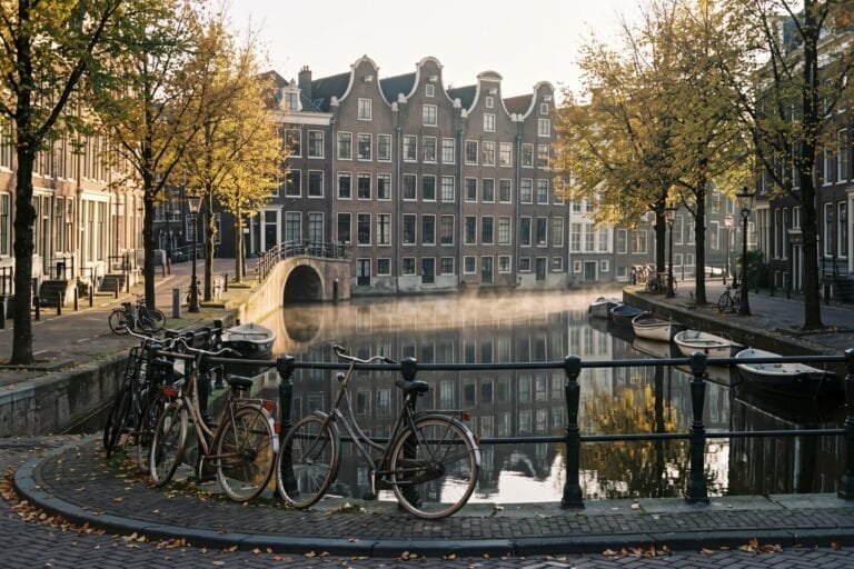 Stenen brug met fietsen over een Amsterdamse gracht met grachtenpanden in het ochtendlicht