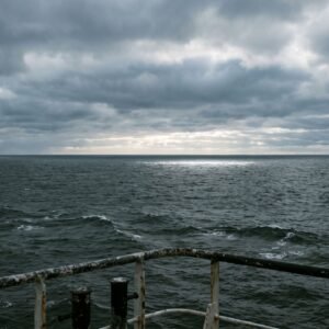 Deining op open zee tot aan de horizon, gezien over de reling van een schip onder een grijze wolkenlucht