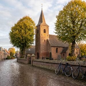 Bakstenen dorpskerk met spitse toren tussen herfstbomen in een Nederlands dorp in de ochtend
