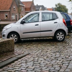 Rij geparkeerde autos van opzij gezien langs een gracht met herfstbladeren op de kade en een fietser op de achtergrond