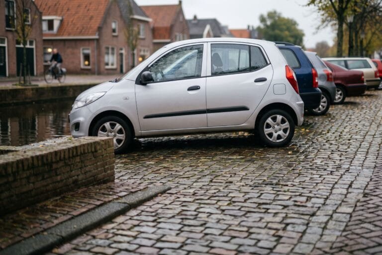 Rij geparkeerde autos van opzij gezien langs een gracht met herfstbladeren op de kade en een fietser op de achtergrond