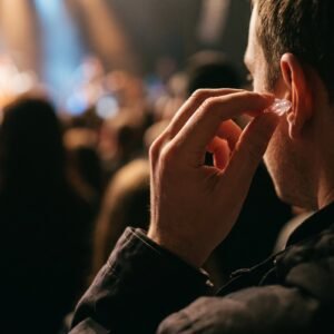 Hand doet een doorzichtige oordop in een oor in een concertzaal met wazig podiumlicht op de achtergrond