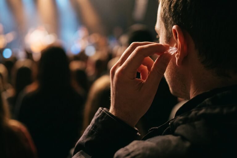 Hand doet een doorzichtige oordop in een oor in een concertzaal met wazig podiumlicht op de achtergrond