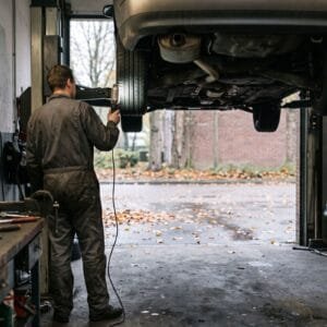 Monteur in overall schijnt met een looplamp onder een auto op een hefbrug in een kleine garage