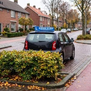 Lesauto met een blauw rijschoolbord op het dak wacht bij een kruising in een woonwijk van achteren gezien