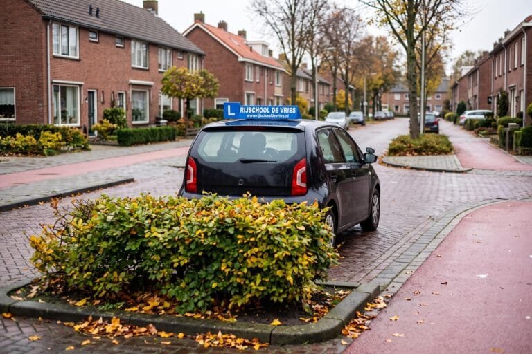Lesauto met een blauw rijschoolbord op het dak wacht bij een kruising in een woonwijk van achteren gezien