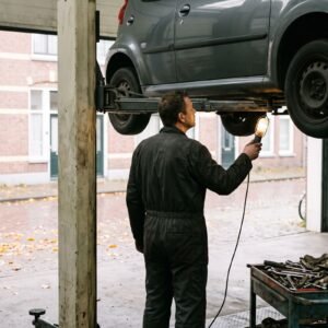 Monteur staat op de rug gezien onder een auto op een brug in een werkplaats met de deur open naar een straat in de herfst