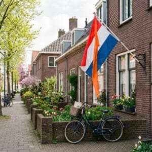 Nederlandse vlag met oranje wimpel aan de gevel van een rijtjeshuis in een rustige straat in het voorjaar