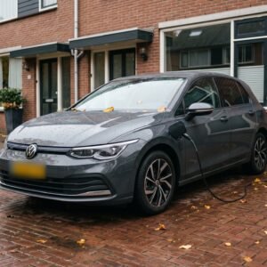 Grijze plug-in hybride laadt via een kabel aan een laadpaal op de gevel, op een oprit voor een rijtjeshuis