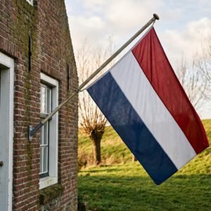 Nederlandse vlag zonder wimpel aan een gevelstok van een bakstenen dijkhuis in laag herfstlicht