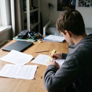 Tiener markeert met een gele stift een zin op een uitgeprinte tekst aan een houten bureau