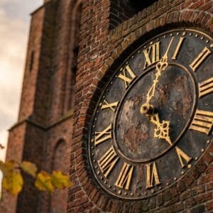 Wijzerplaat van een oude torenklok met vergulde Romeinse cijfers en wijzers in het avondlicht