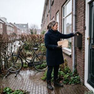 Vrouw in winterjas haalt op een grijze decemberochtend enveloppen uit de brievenbus naast haar voordeur
